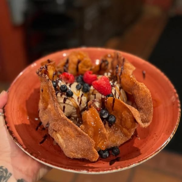 Churro bowl dessert with ice cream, blueberries, raspberries, and chocolate drizzle on a red plate.