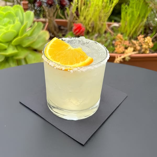 A Hidalgo's Cocina & Cócteles margarita with a salted rim and orange slice on a black napkin.