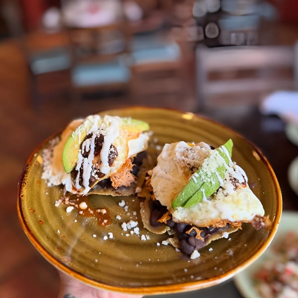 Two Mexican tostadas with black beans, cheese, avocado, and crema on a brown plate.