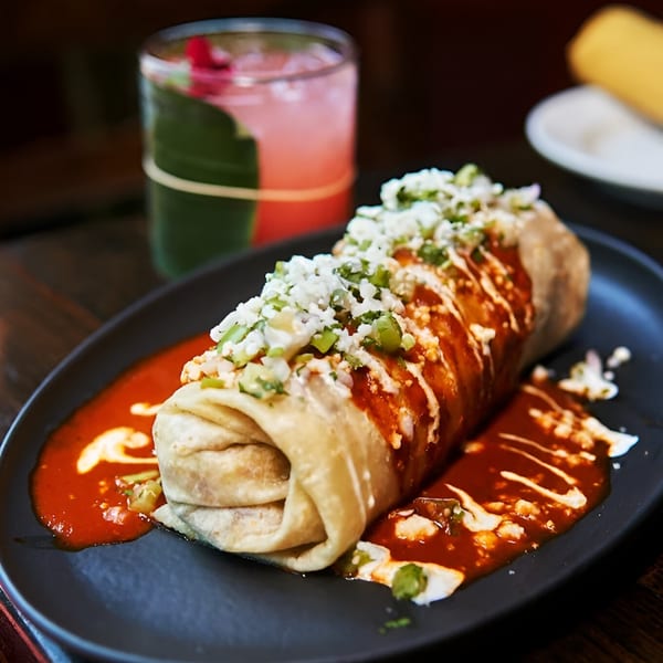 A Hidalgo’s Cocina & Cócteles burrito, topped with cheese and sauce, next to a pink cocktail.