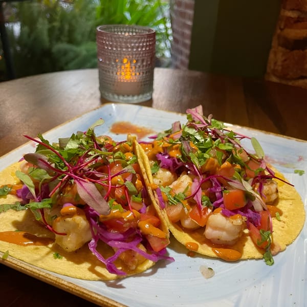 Two vibrant shrimp tacos with red cabbage, tomatoes, and microgreens, next to a lit candle.