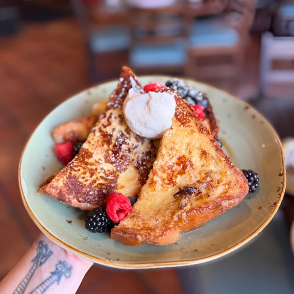 Golden French toast slices topped with whipped cream, powdered sugar, and fresh berries on a green plate.
